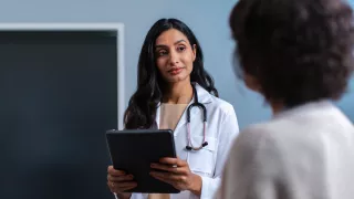 A female doctor in white coat speaks to a patient in a hospital room