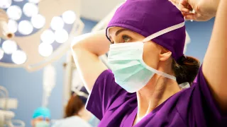Female surgeon secures her face mask in an operating room.