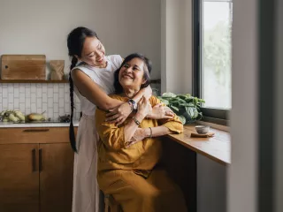 A woman embraces her mother warmly in the kitchen